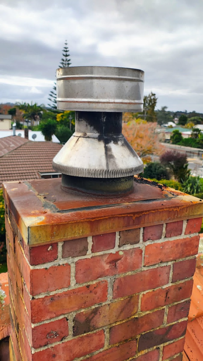 An old, rusty chimney cowl and rusted flashing on a brick chimney — before