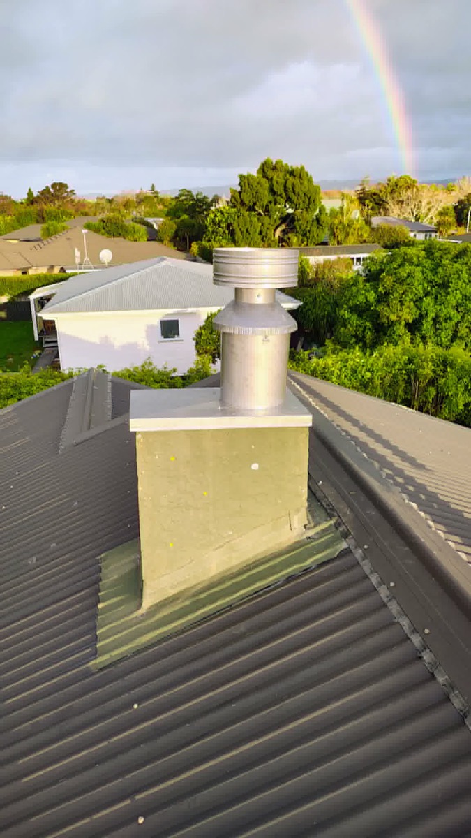 A new stainless flue and cowl capping the chimney — after, with a rainbow behind