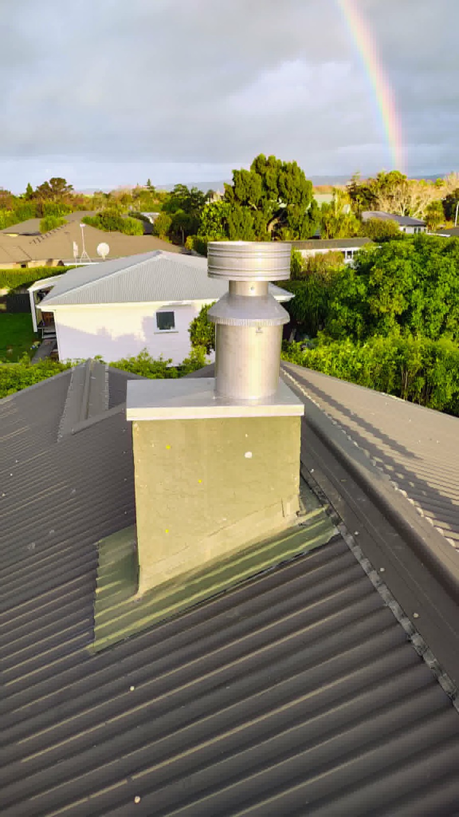 A new stainless flue and rain cap on a metal roof with a rainbow behind